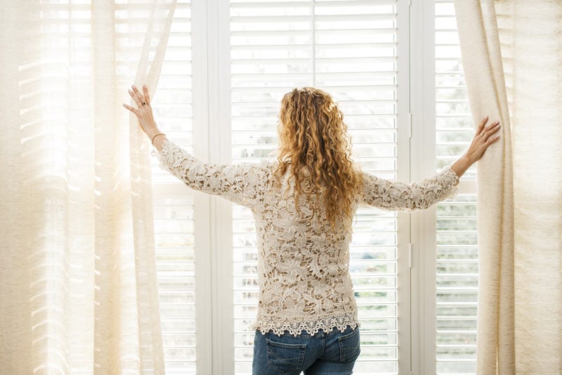 young lady opening window curtains in bedroom